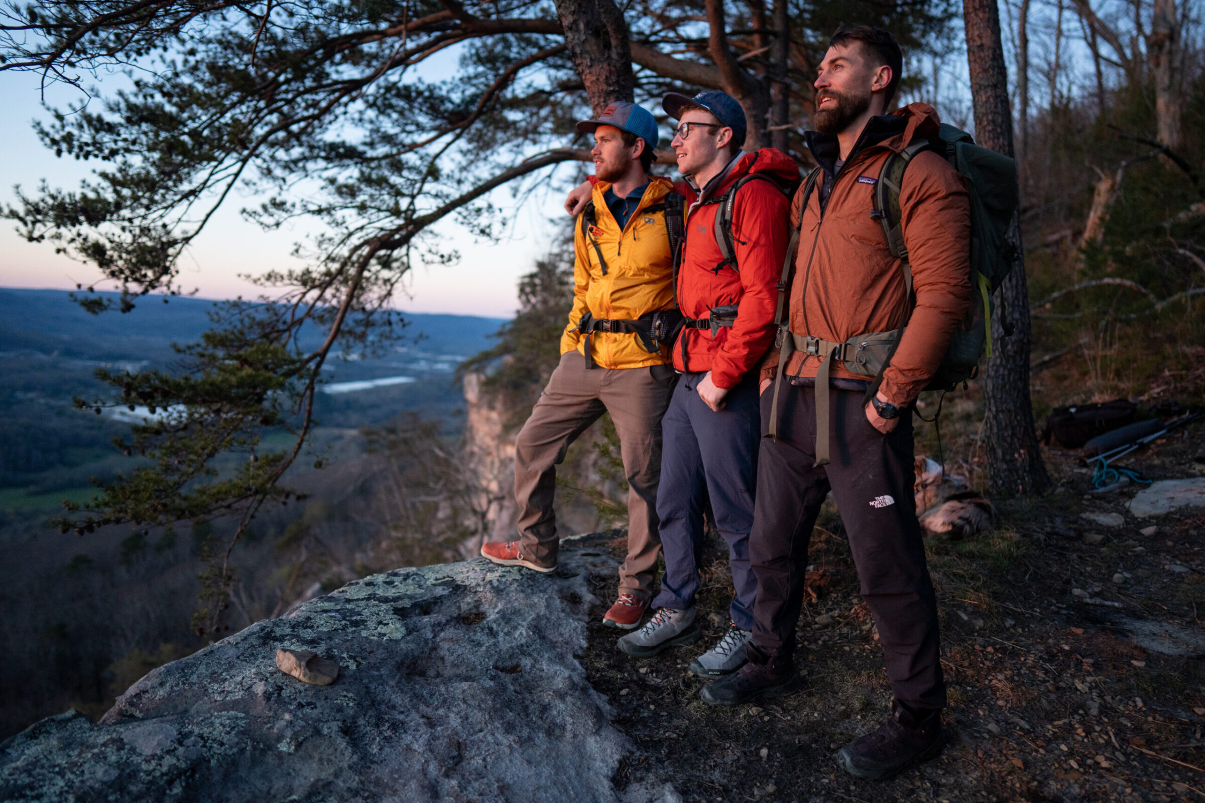 Three guys stand on an overlook while wearing windbreaker jackets