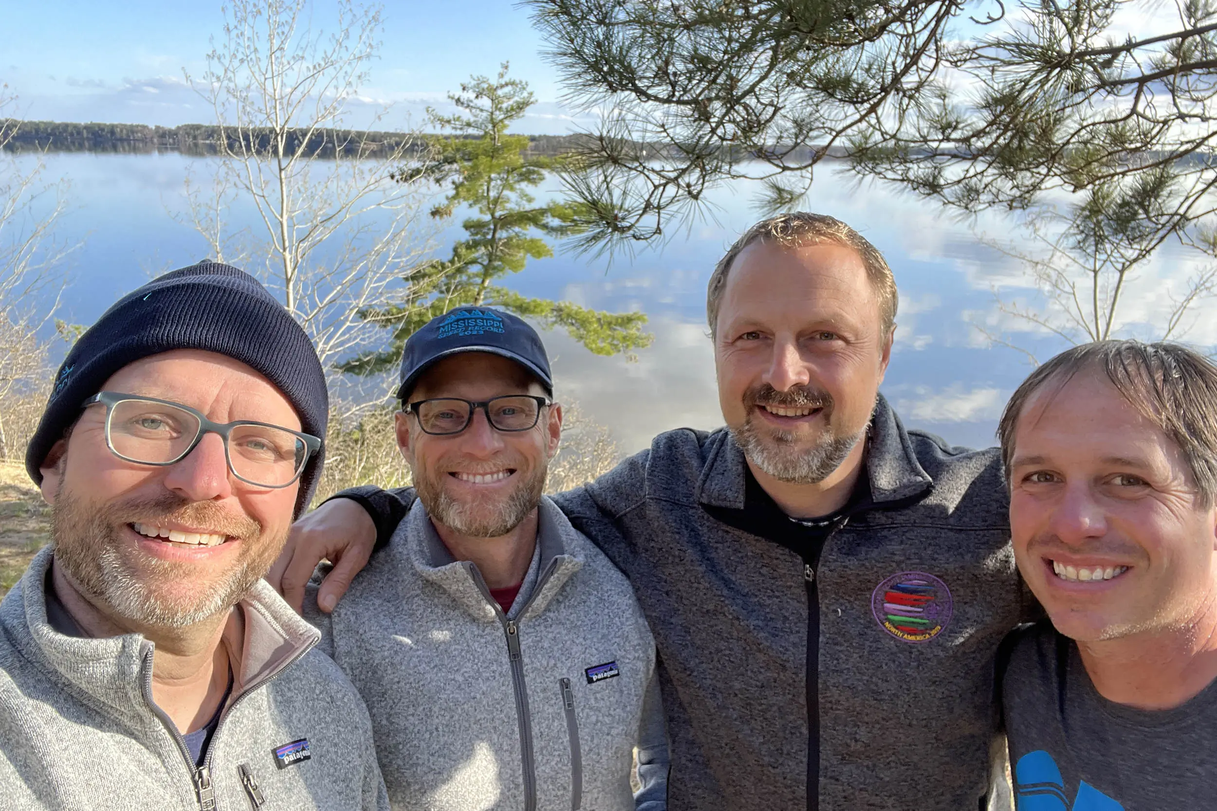 four men stand side by side with arms around each others shoulders