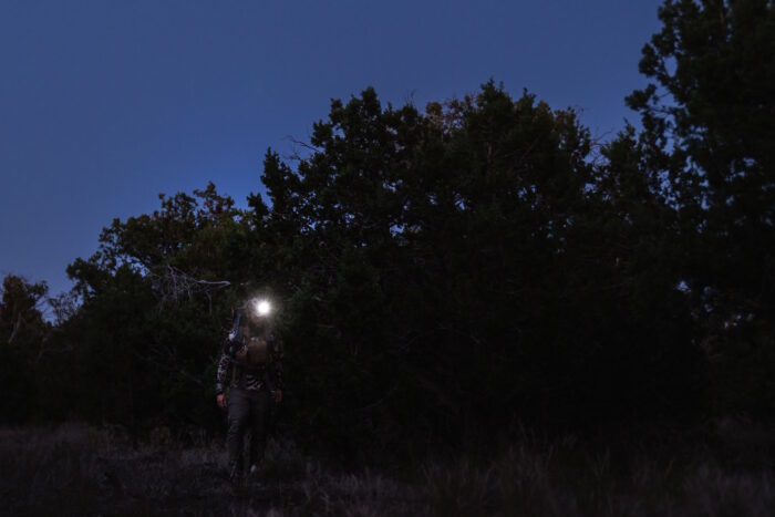 man wearing a headlamp shines a light in a dark forest
