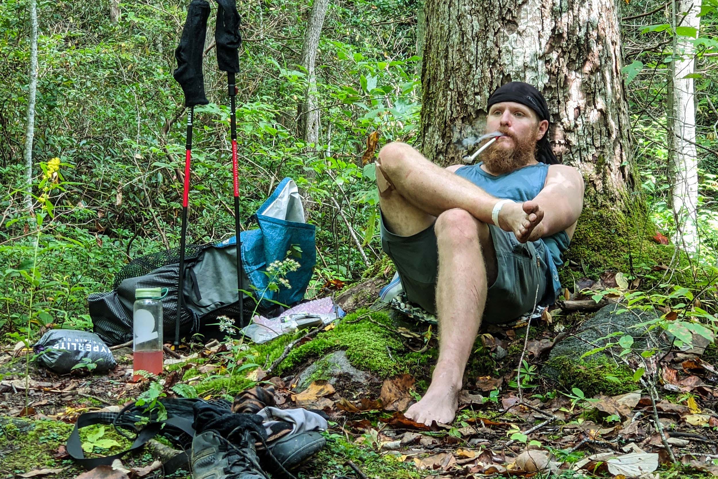 tired hiker sitting next to a tree in the woods