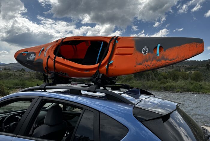 a pyranha kayak loaded onto kuat kayak roof rack on a blue car