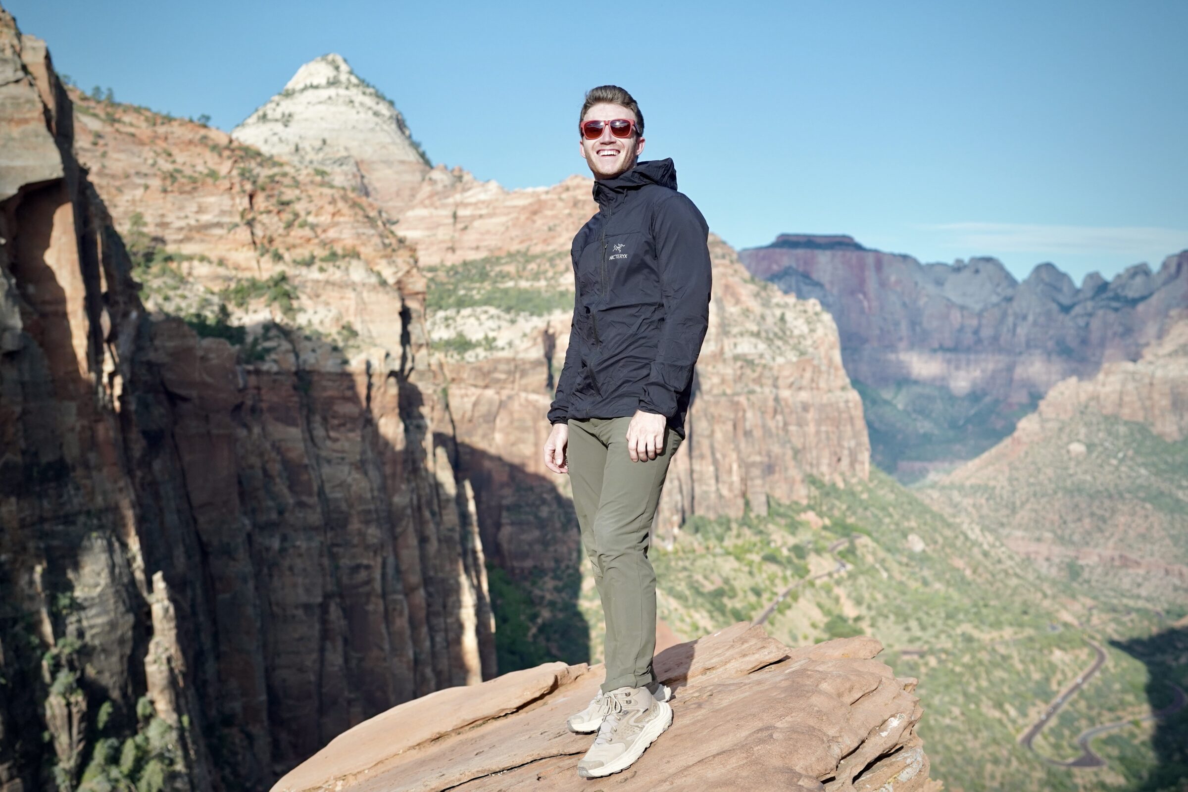 A man stands at an overlook while wearing a windbreaker jacket