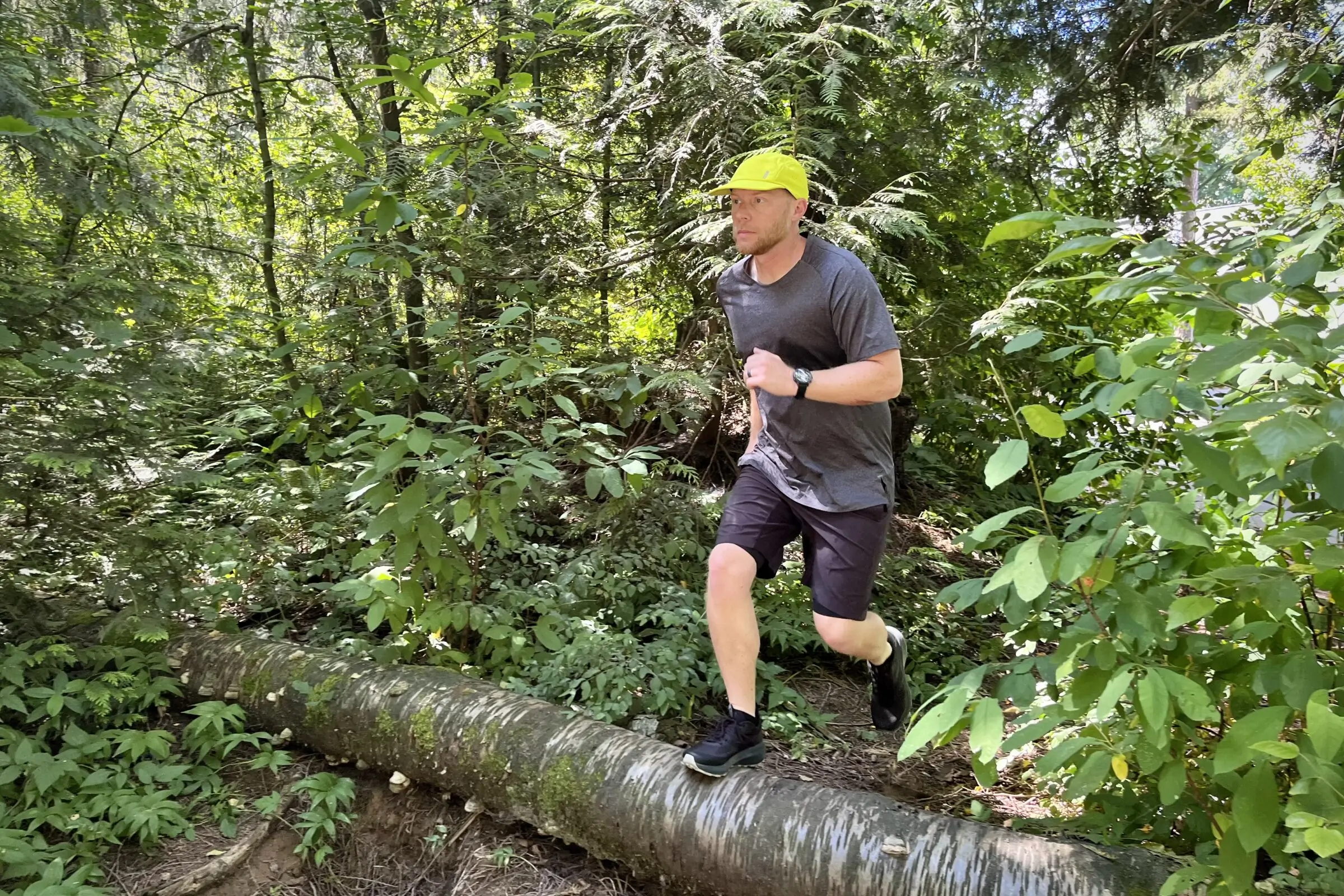 A man runs over a log while wearing a running hat