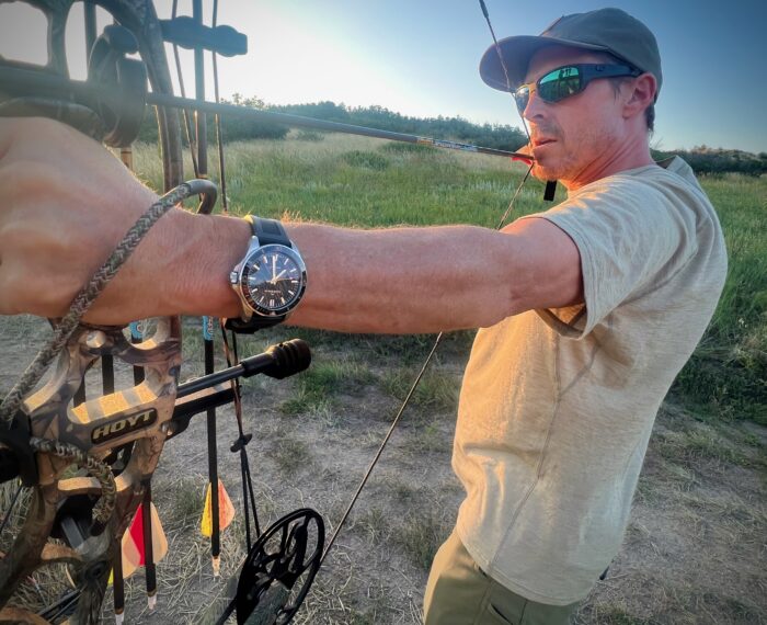 A man wears a The NORQAIN Neverest Glacier watch while drawing a bow