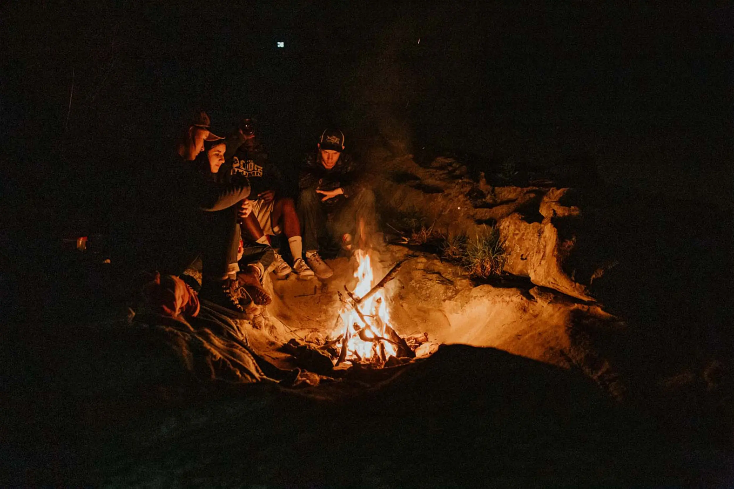 a group of people sits around a fire at the beach