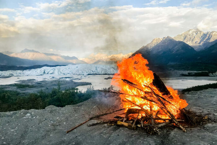 a large fire by a pond with mountains in the background