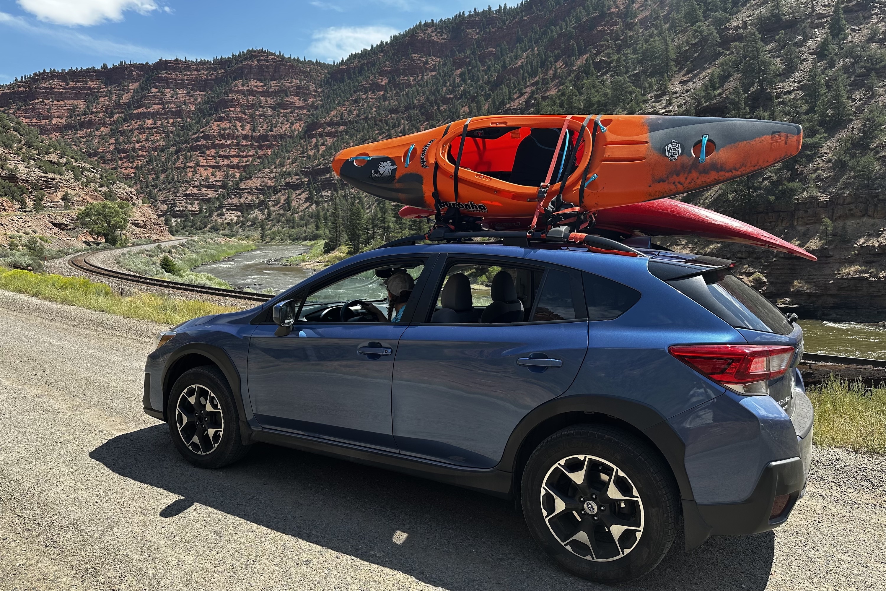 A Subaru car driving along a dirt road for river access with a orange kayak on a Kuat roof rack