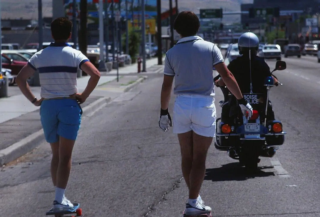 two skateboarders ride behind a police motorcycle in Boise, Idaho in 1984. 
