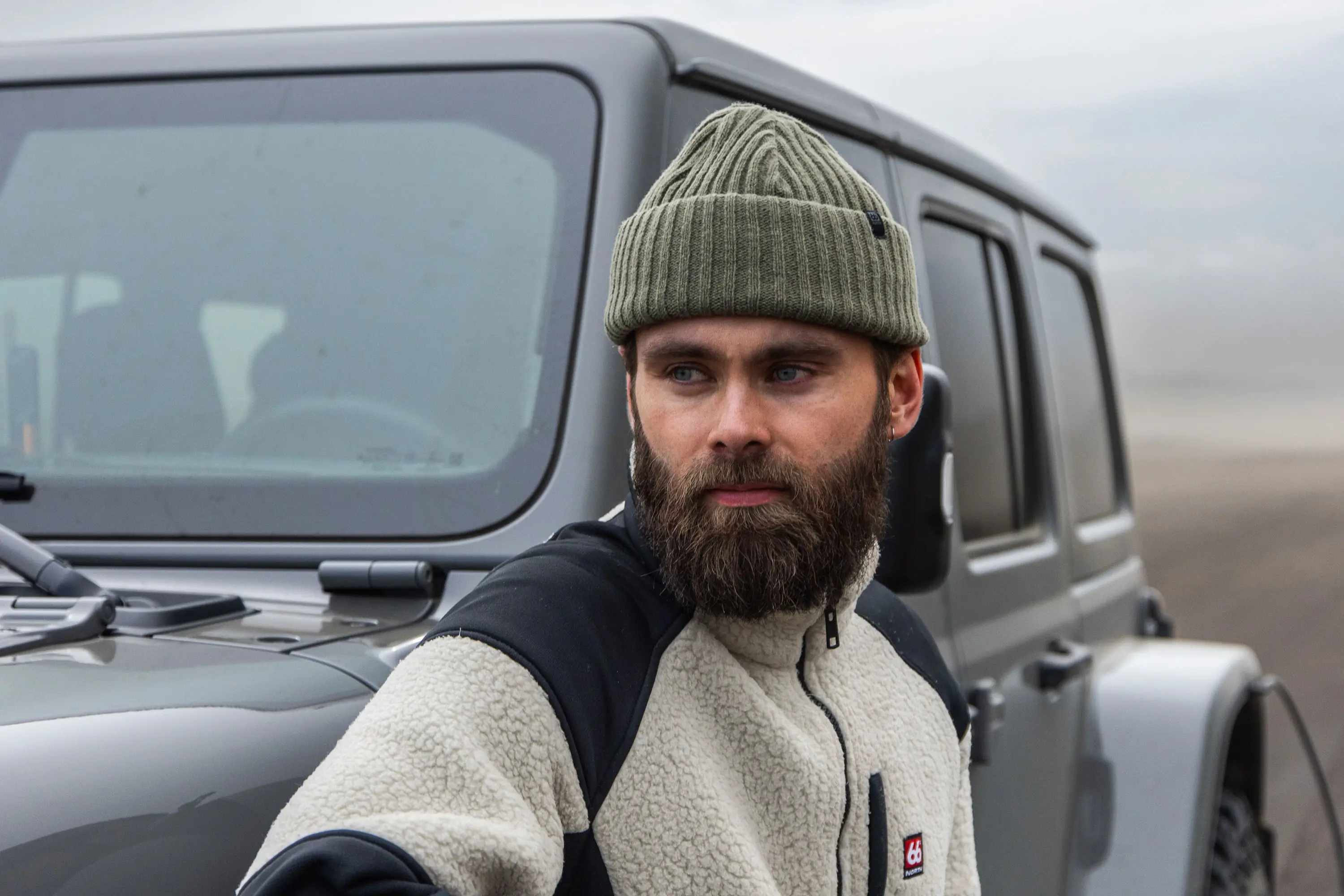 man with beard and 66 north beanie standing next to a Jeep