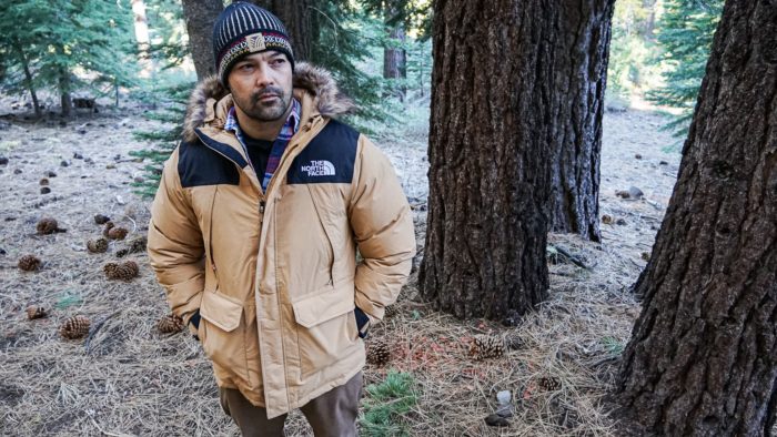 A handsome man models The North Face McMurdo Down Parka in a wooded setting.