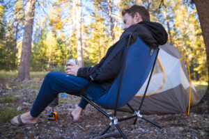 A man sits in a backpacking chair at a campsite