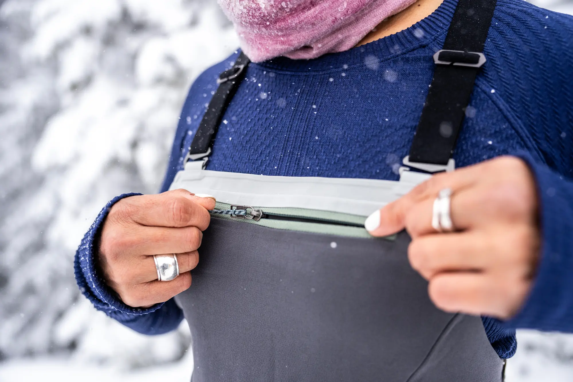 woman pulls zipper tab on chest pocket on ski bibs