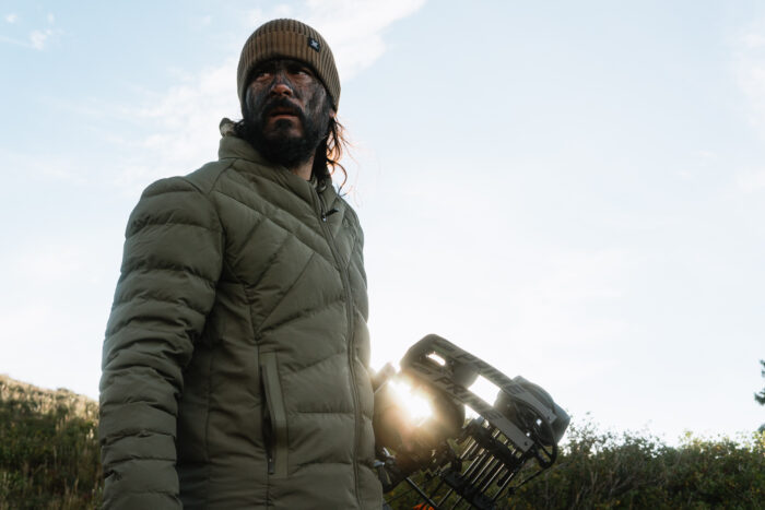 author wearing pnuma's Weekender Jacket while holding a bow on a sunny hunting trip