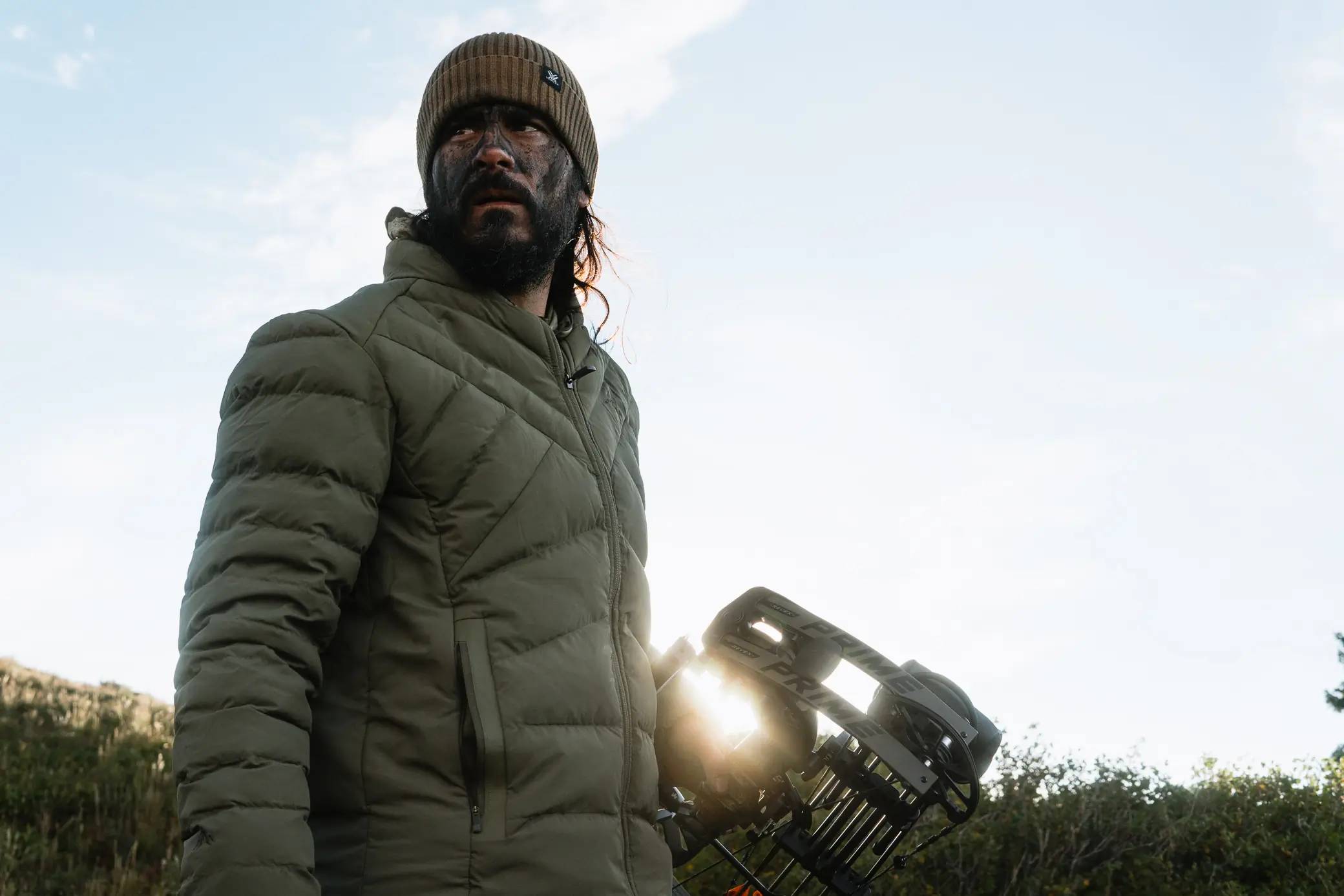 author wearing pnuma's Weekender Jacket while holding a bow on a sunny hunting trip