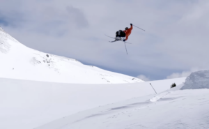 a skier in a red jacket executing a flip off a snowy jump