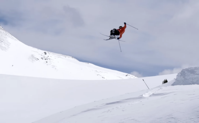 a skier in a red jacket executing a flip off a snowy jump