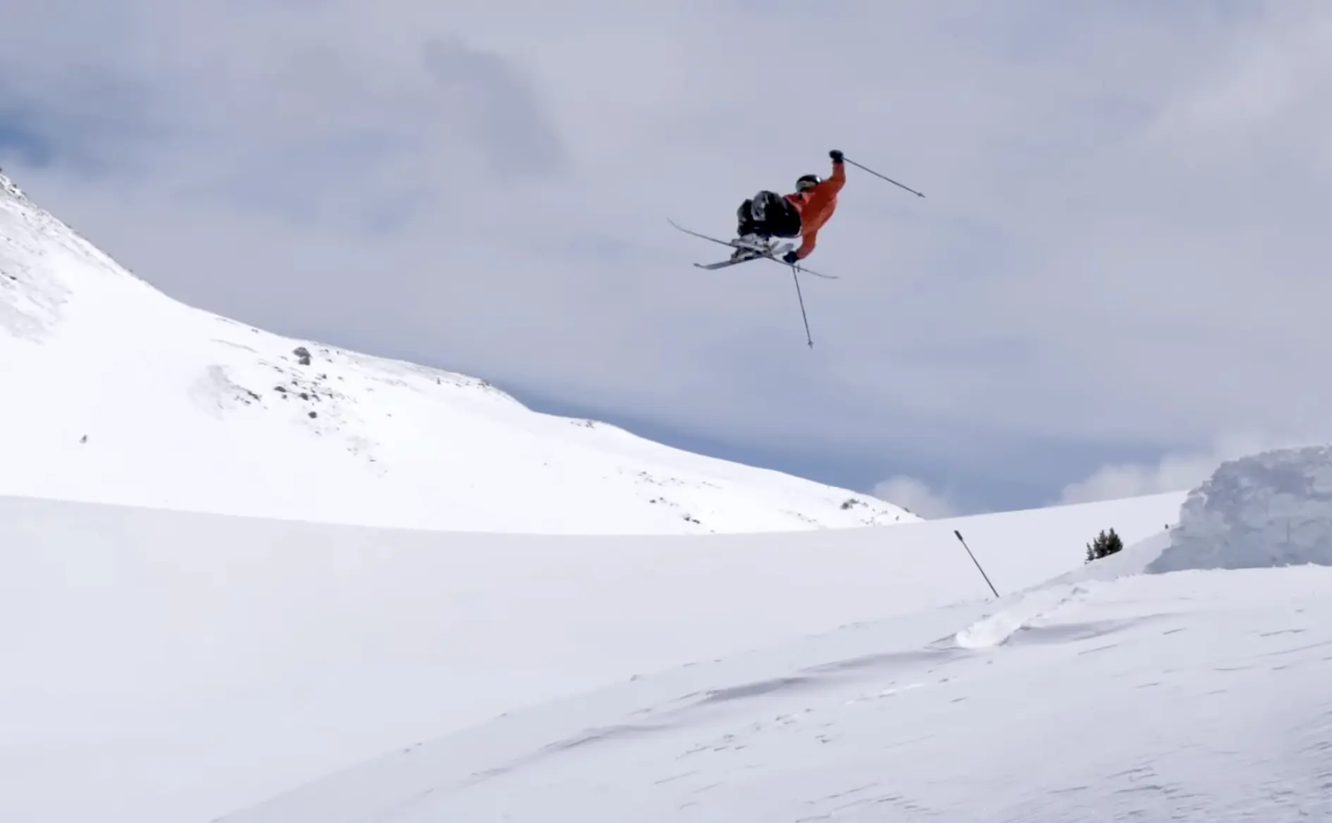 a skier in a red jacket executing a flip off a snowy jump