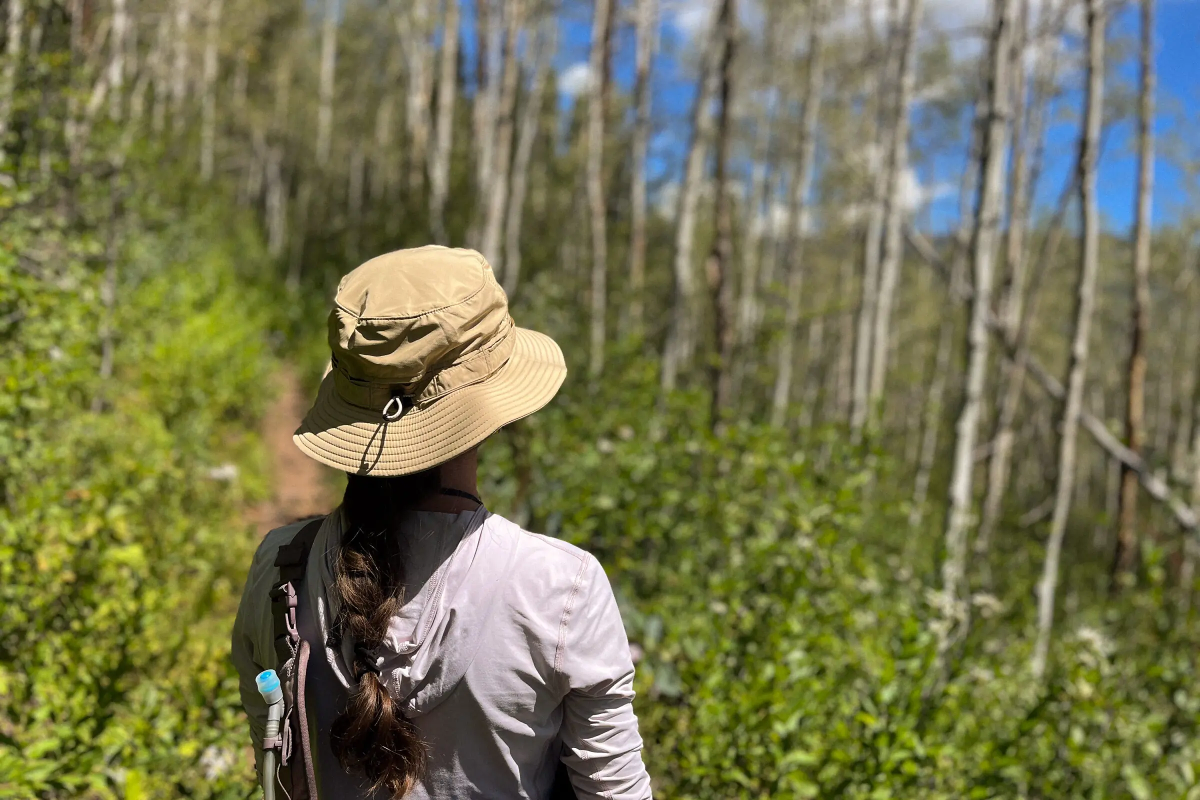 A woman walks down a trail while wearing a sun hat