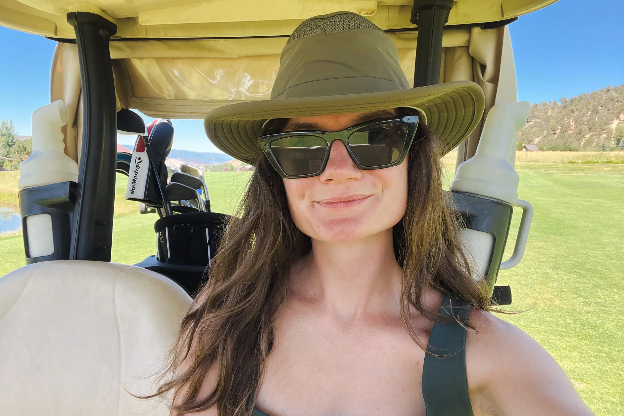 A woman sits in a golf cart while wearing a sun hat