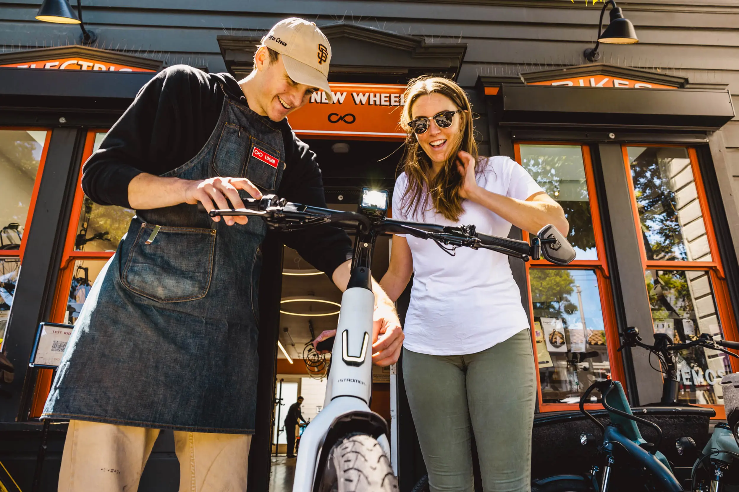a man and a woman hold the handlebars of an e-bike in front of a bike store