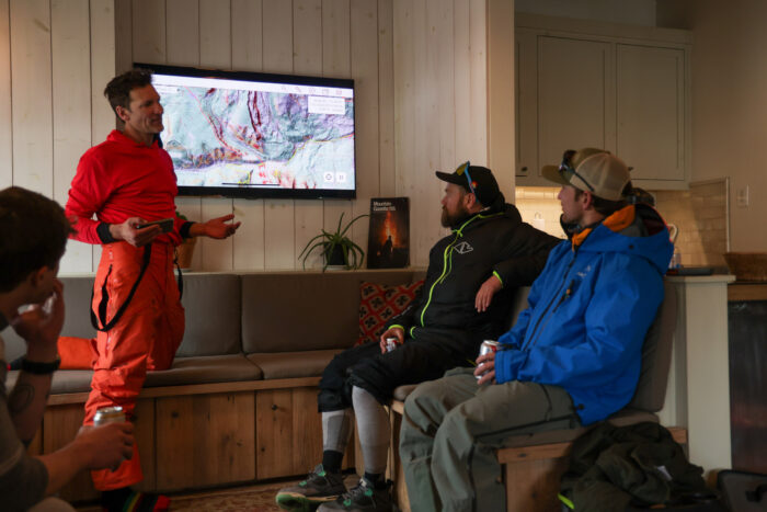 Person explain how to use the avalanche safety prevention app to a team of skiers