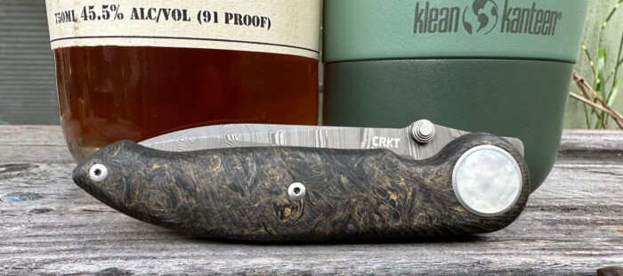 crkt pursue knife displayed over a wood table in front of two bottles