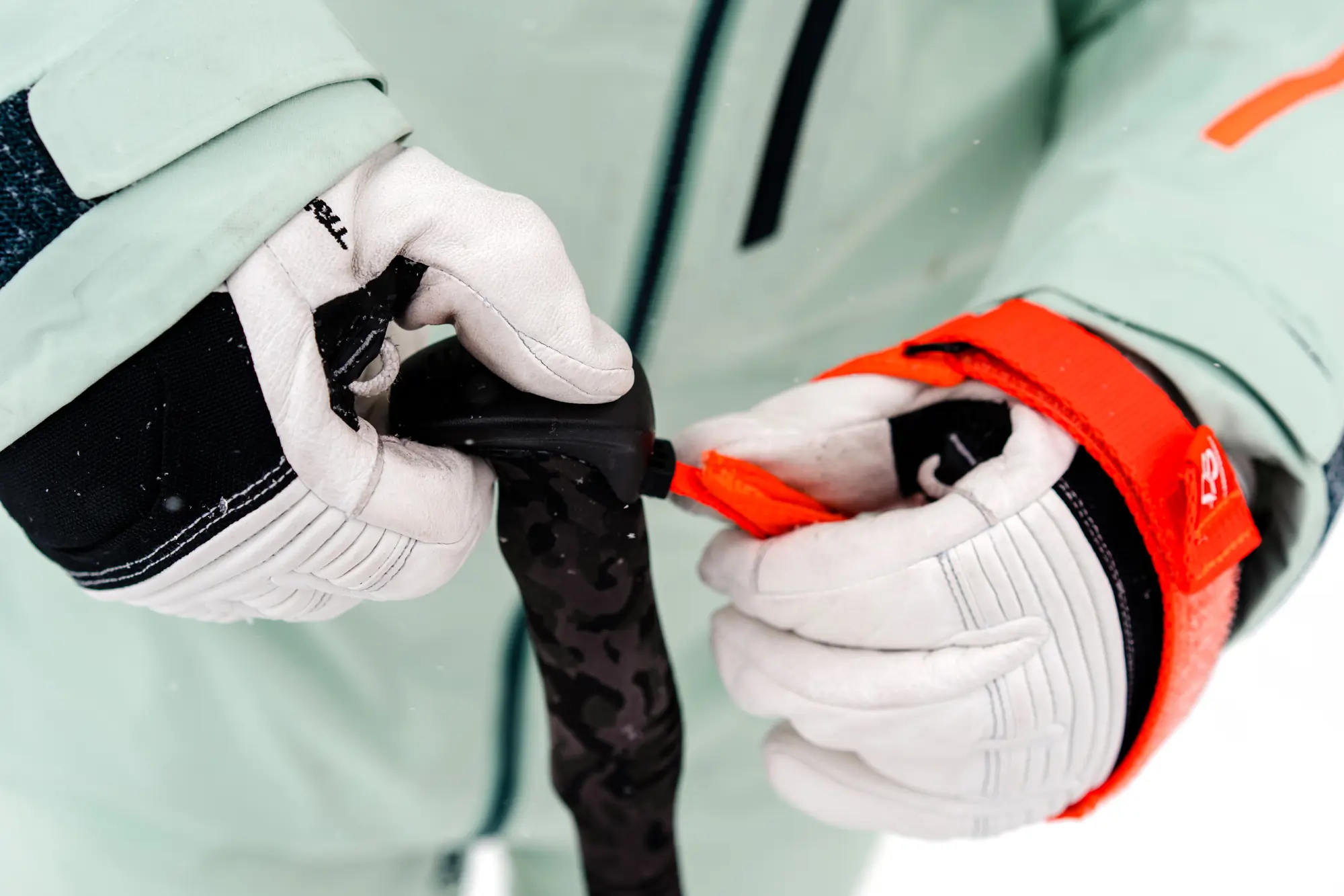 person adjusting a ski pole strap with ski gloves on 