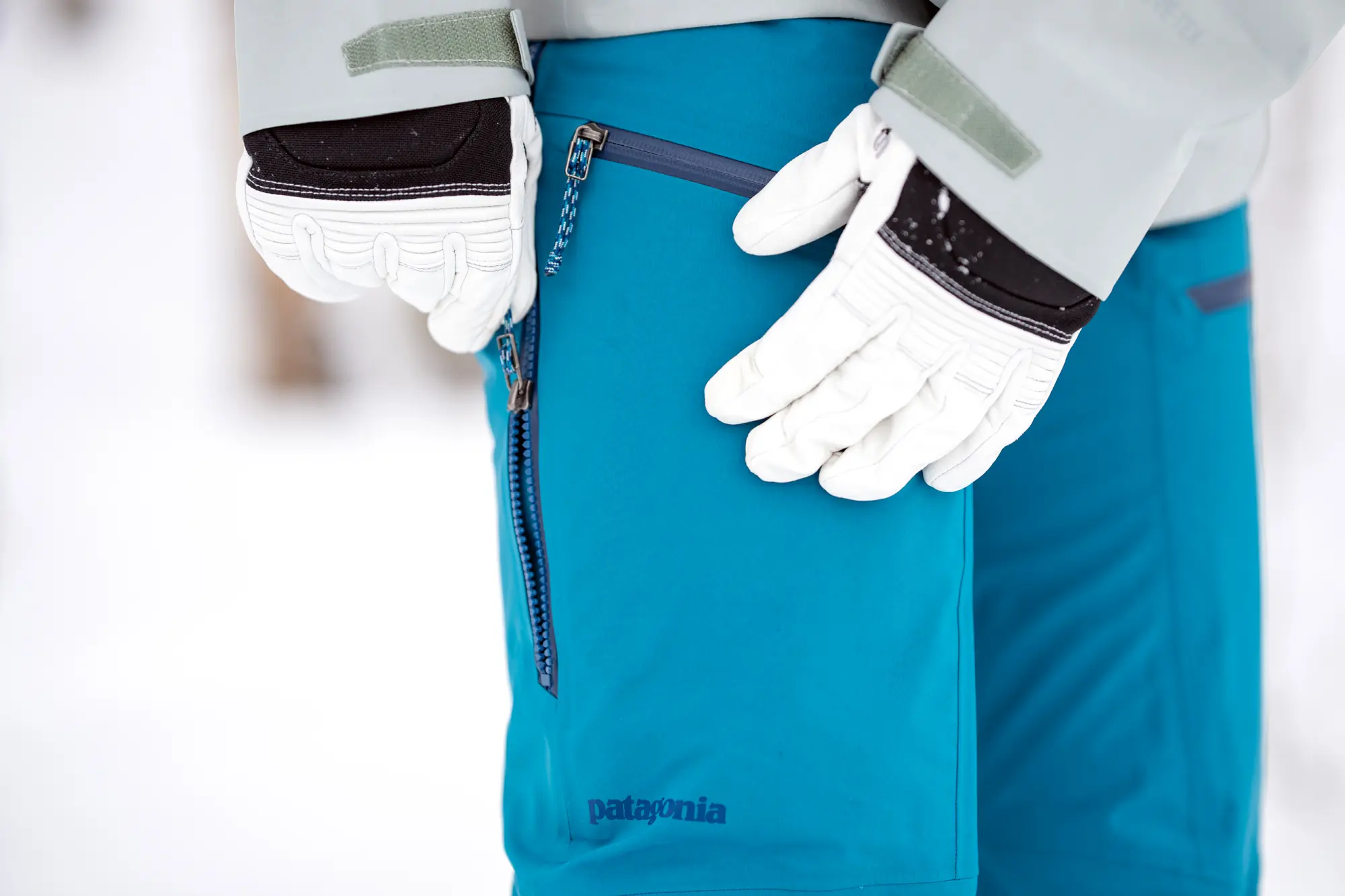 woman pulling up size zipper on ski pants with white ski gloves on