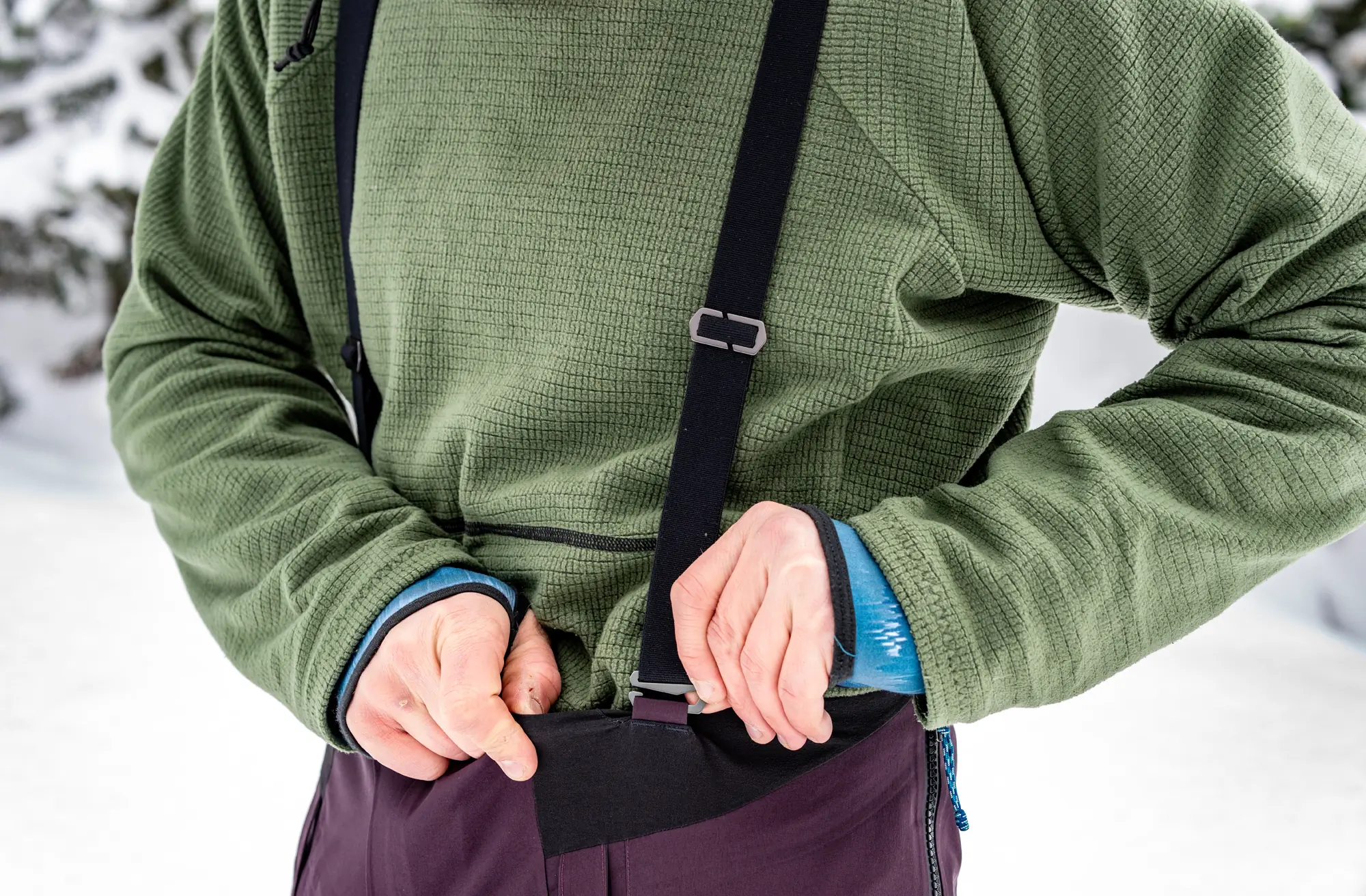 man removing suspender at waist attachment on ski bibs 