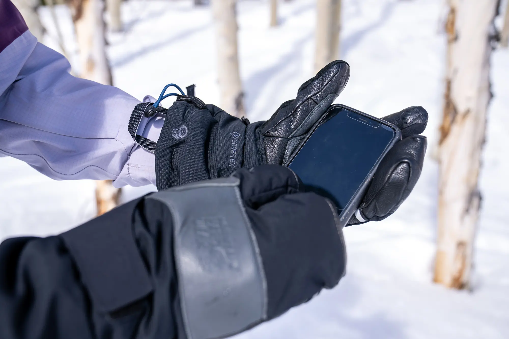 holding phone in hands while wearing winter mittens 