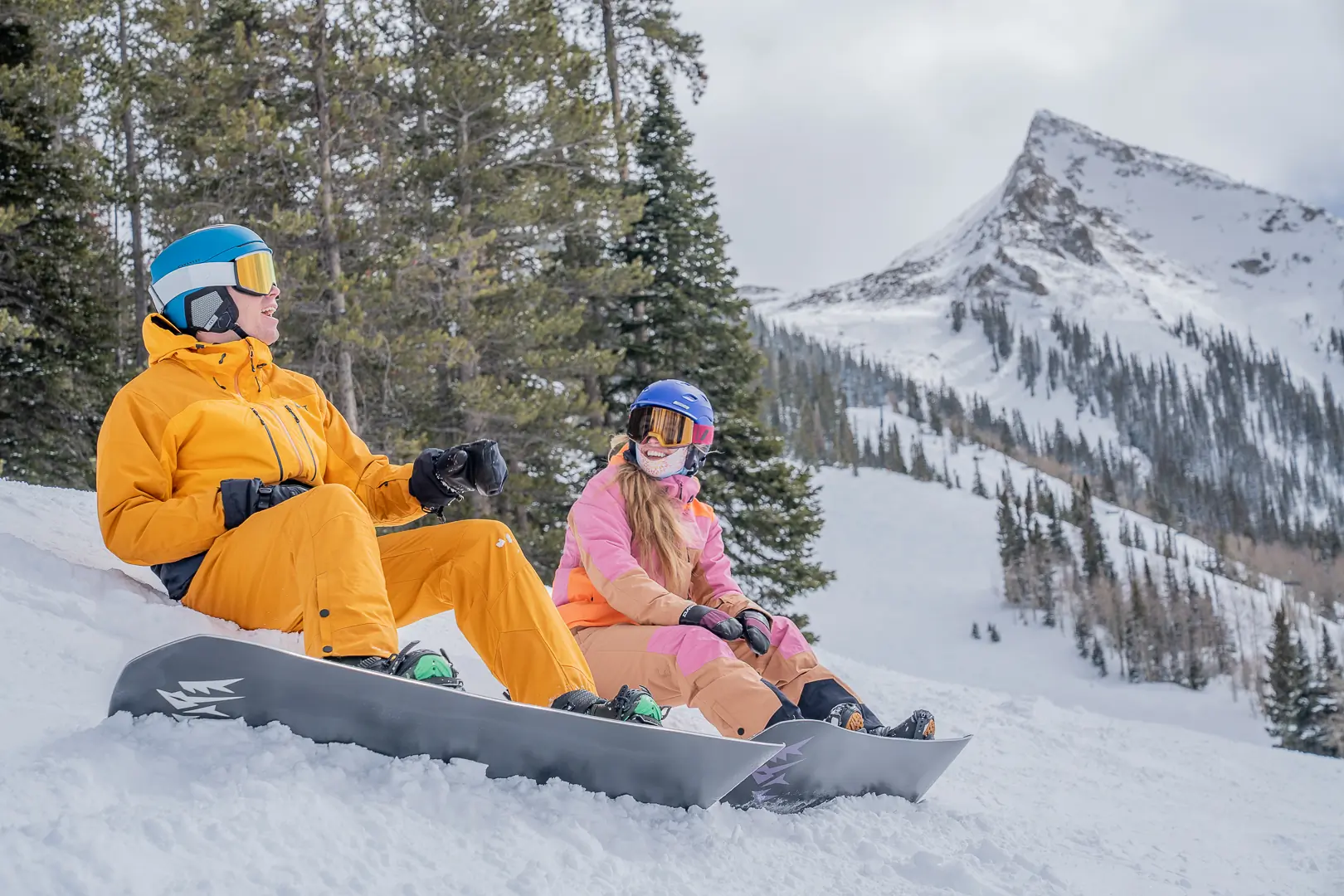 two snowboarders sitting on the side of the run at Crested Butte Mountain Resort with peak in background 