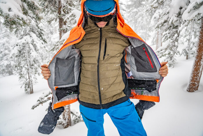 snowboarder opening up jacket and wearing puffy jacket beneath 