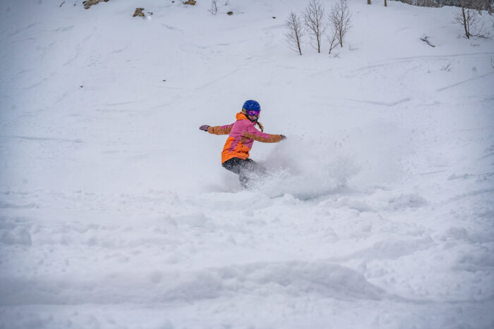 snowboarder takes turns through deep snow with an orange-pink jacket