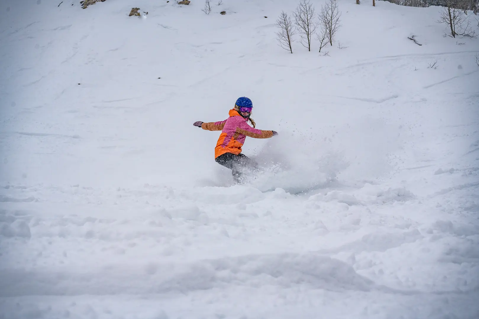 snowboarder takes turns through deep snow with an orange-pink jacket