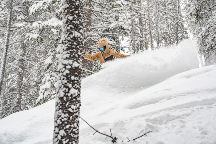 snowboarder making big slash in powder field in the trees 