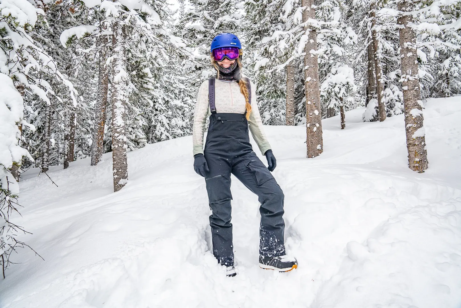 female snowboarder standing in ski bibs and long sleeve base layer top