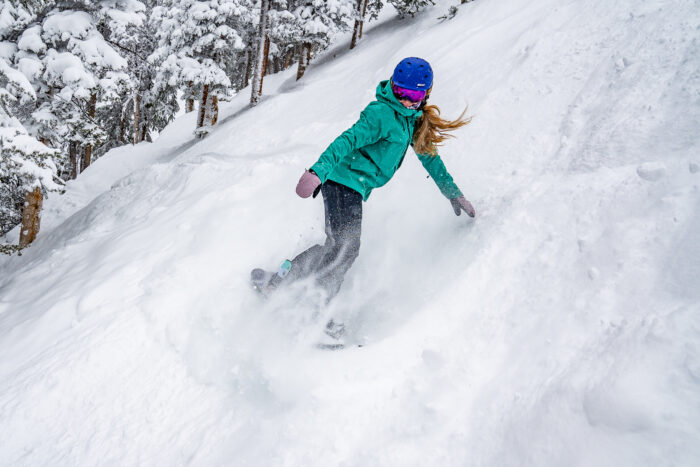 snowboarder taking slash on a steep, choppy powder slope