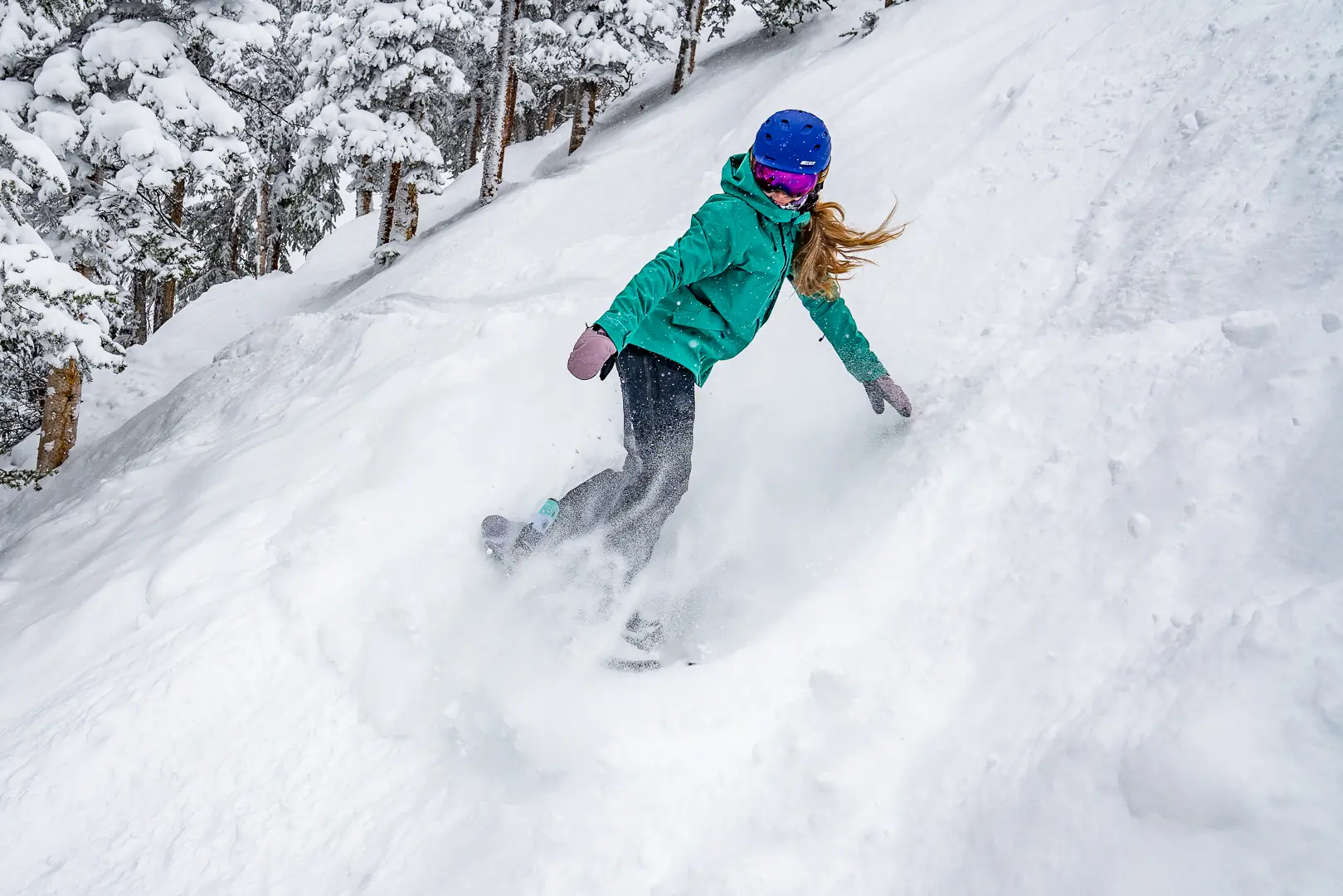 snowboarder taking slash on a steep, choppy powder slope