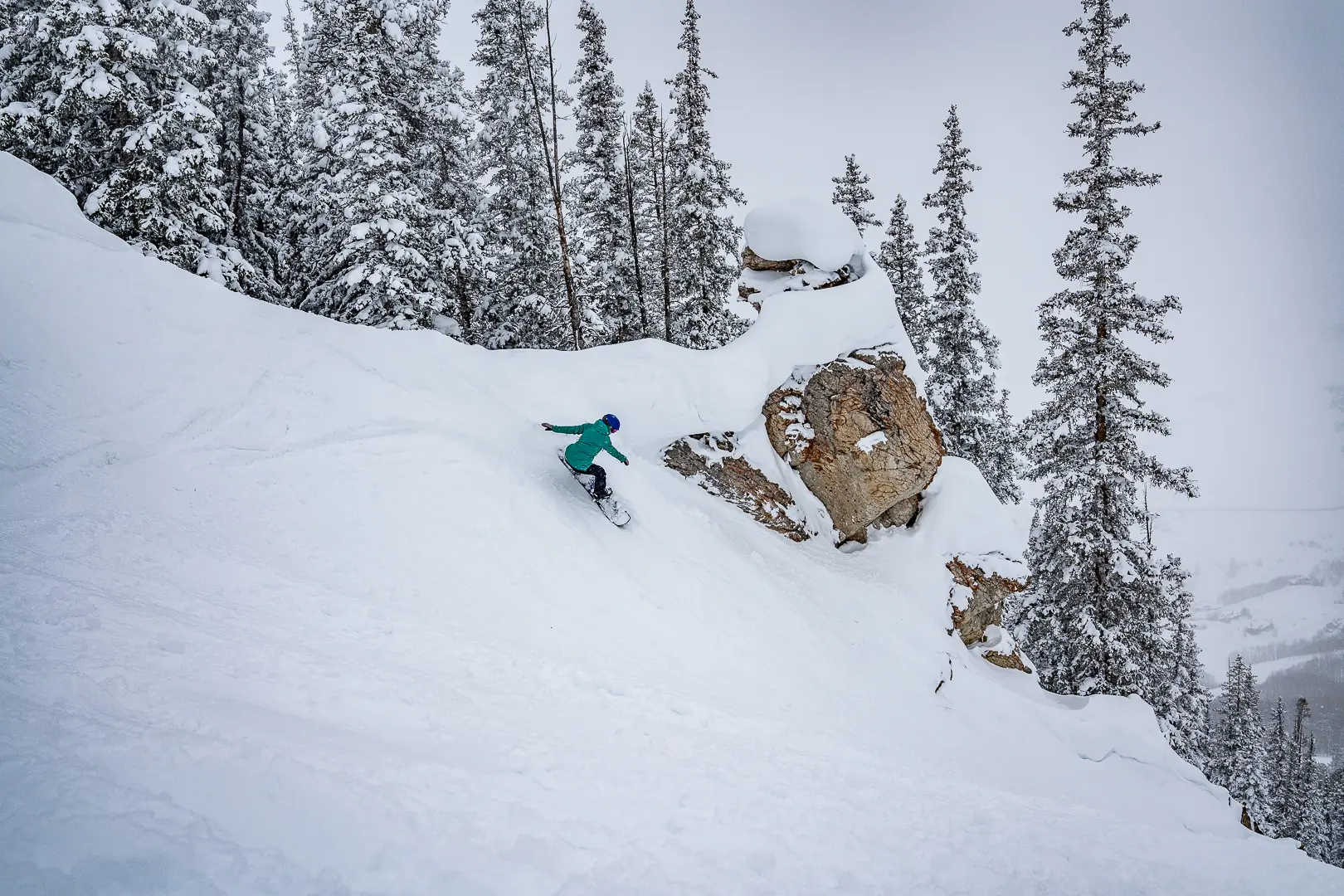 snowboarder takes steep turn beneath rock feature on a powder day 