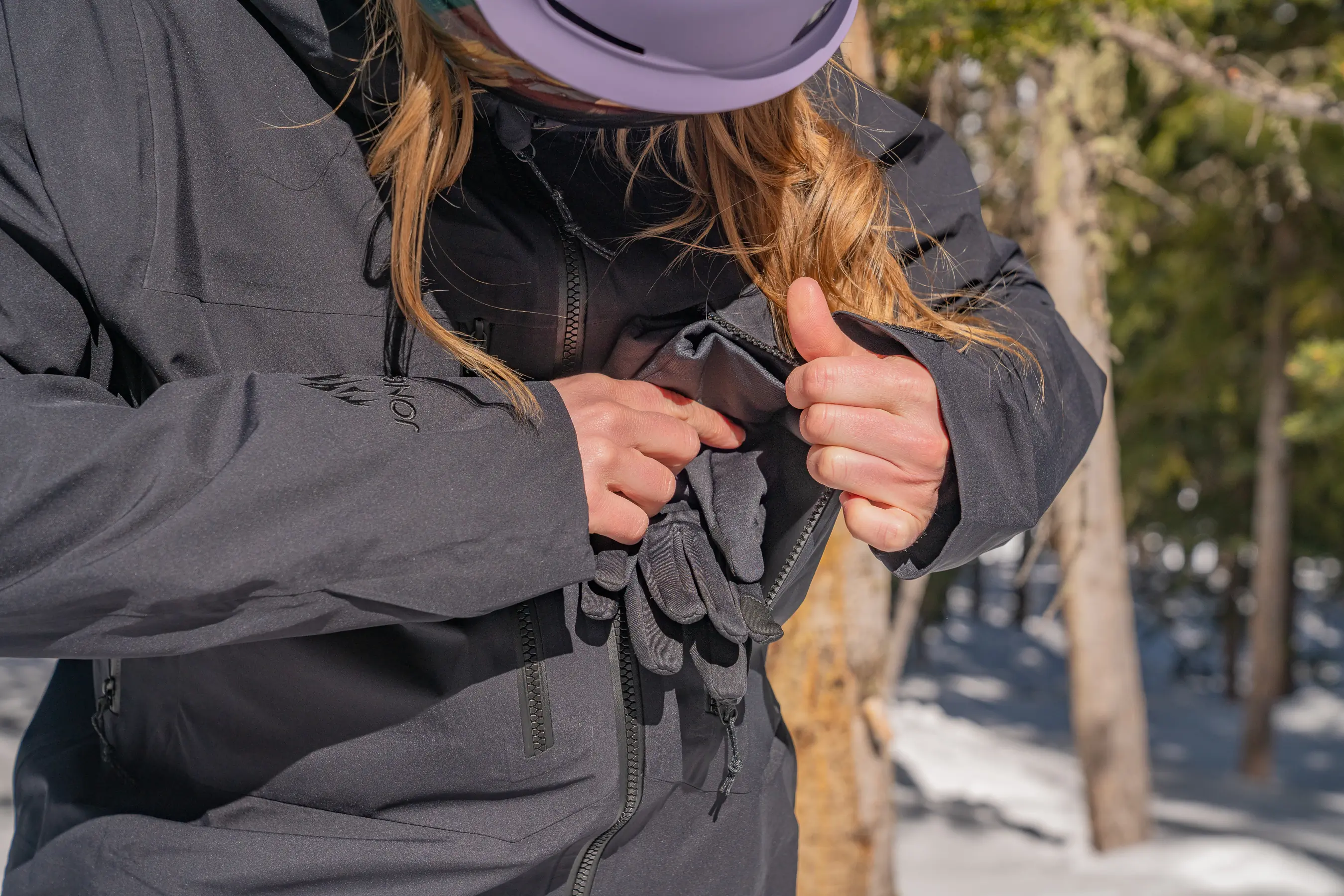 woman putting glove liners into exterior chest pocket 