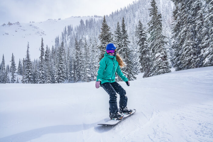 snowboarder coasts on a flat trail beneath a steep run 