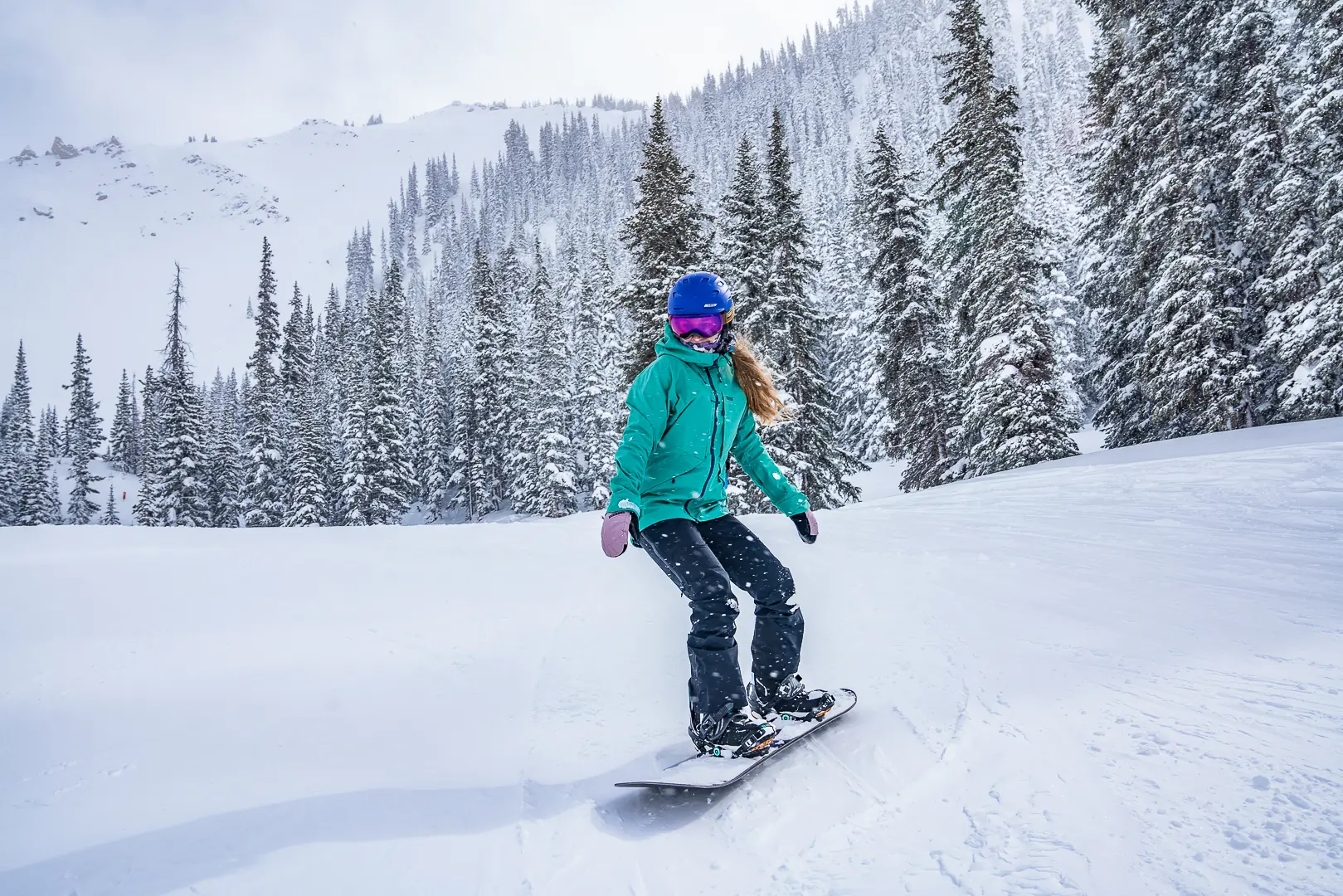 snowboarder coasts on a flat trail beneath a steep run 