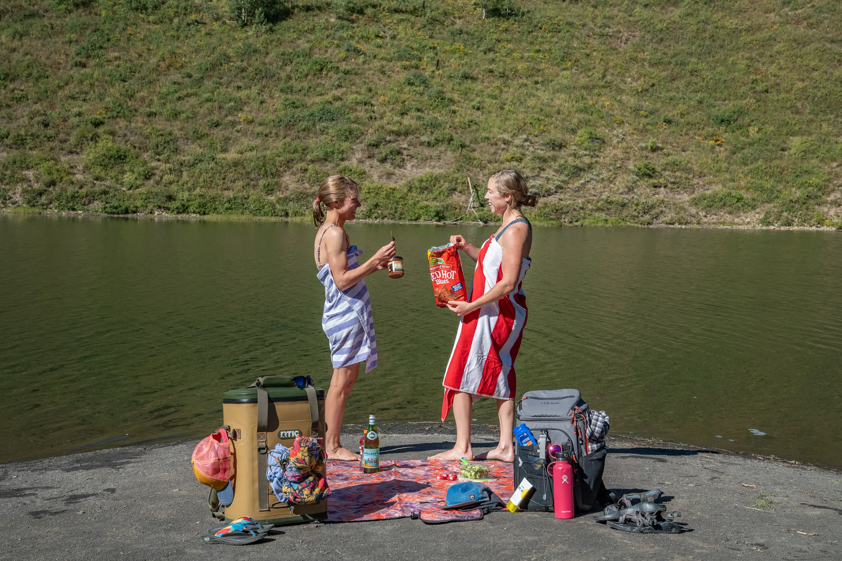 two women standing in beach towels having a snack