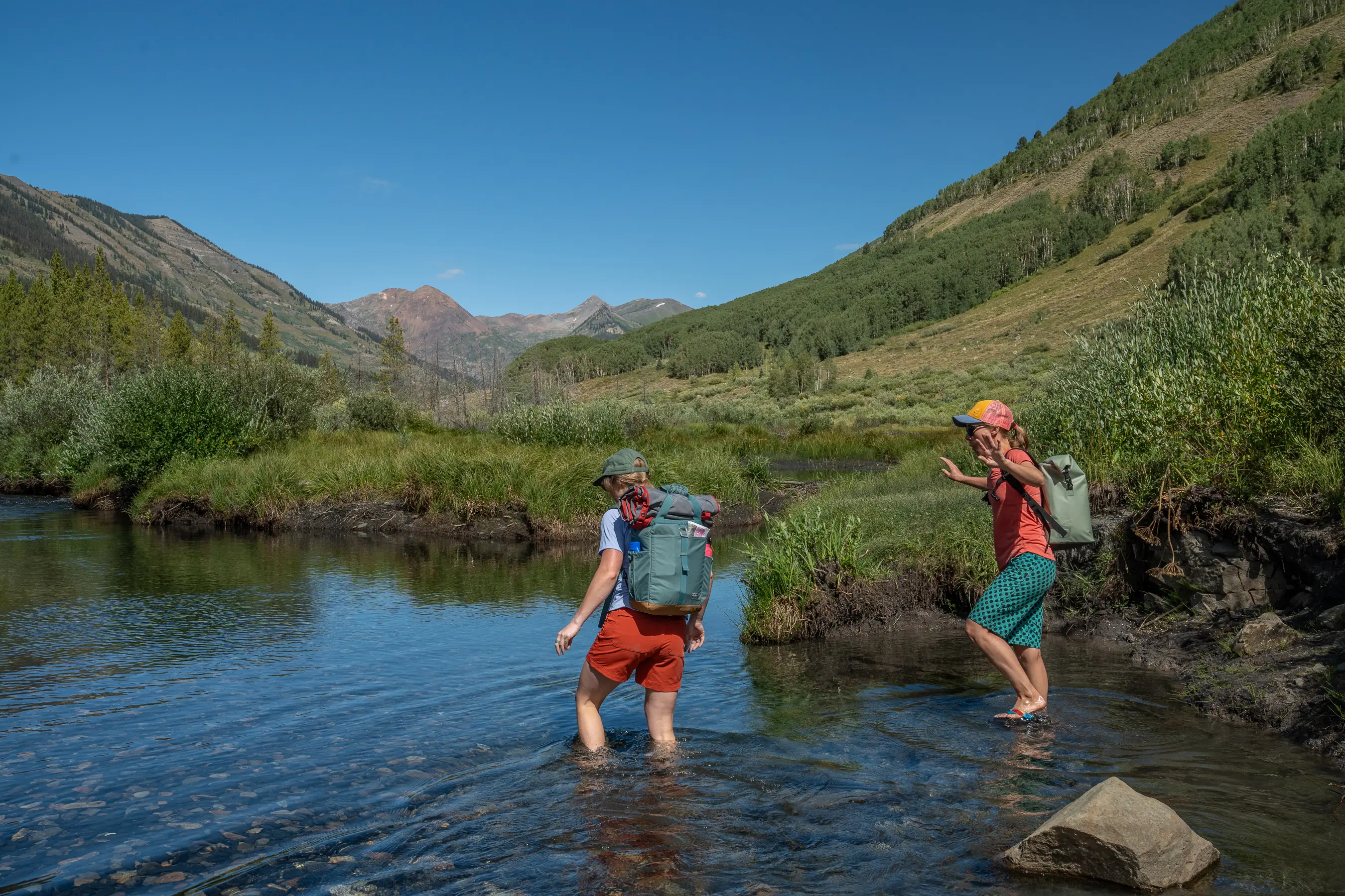 two women crossing creek with packs on