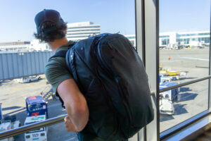 Peak Design Travel Backpack on the Back of a Traveller in Seattle International Airport Looking out on the Tarmac.