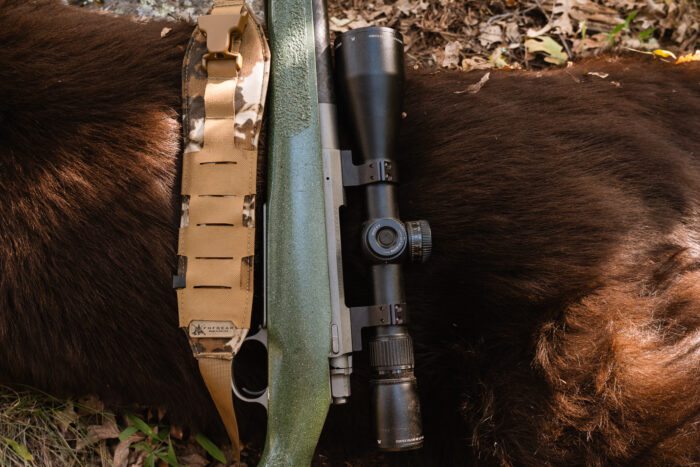 rifle and sling resting on body of hunted bear