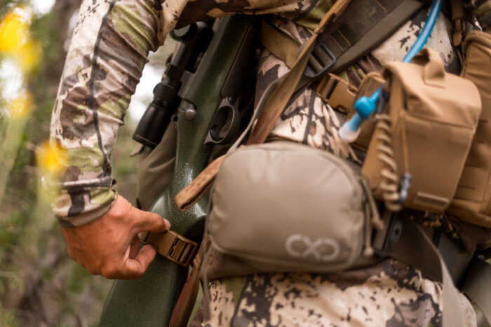 Hunter clipping his rifle sling to his backpack using the pack attachment feature of the sling