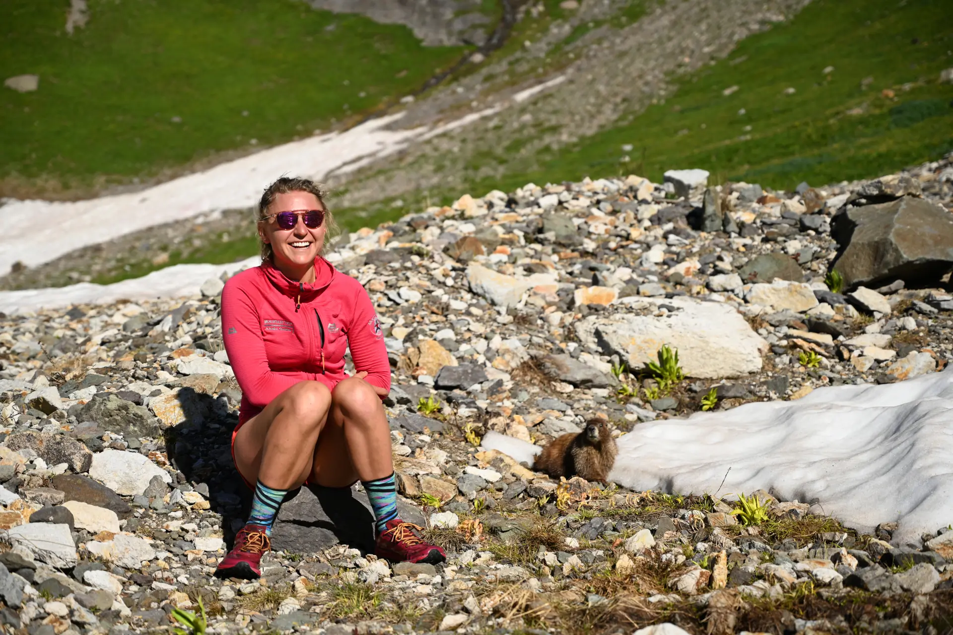 GearJunkie author Kaylee Walden in a fleece and running shorts sitting on a rock in the alpine