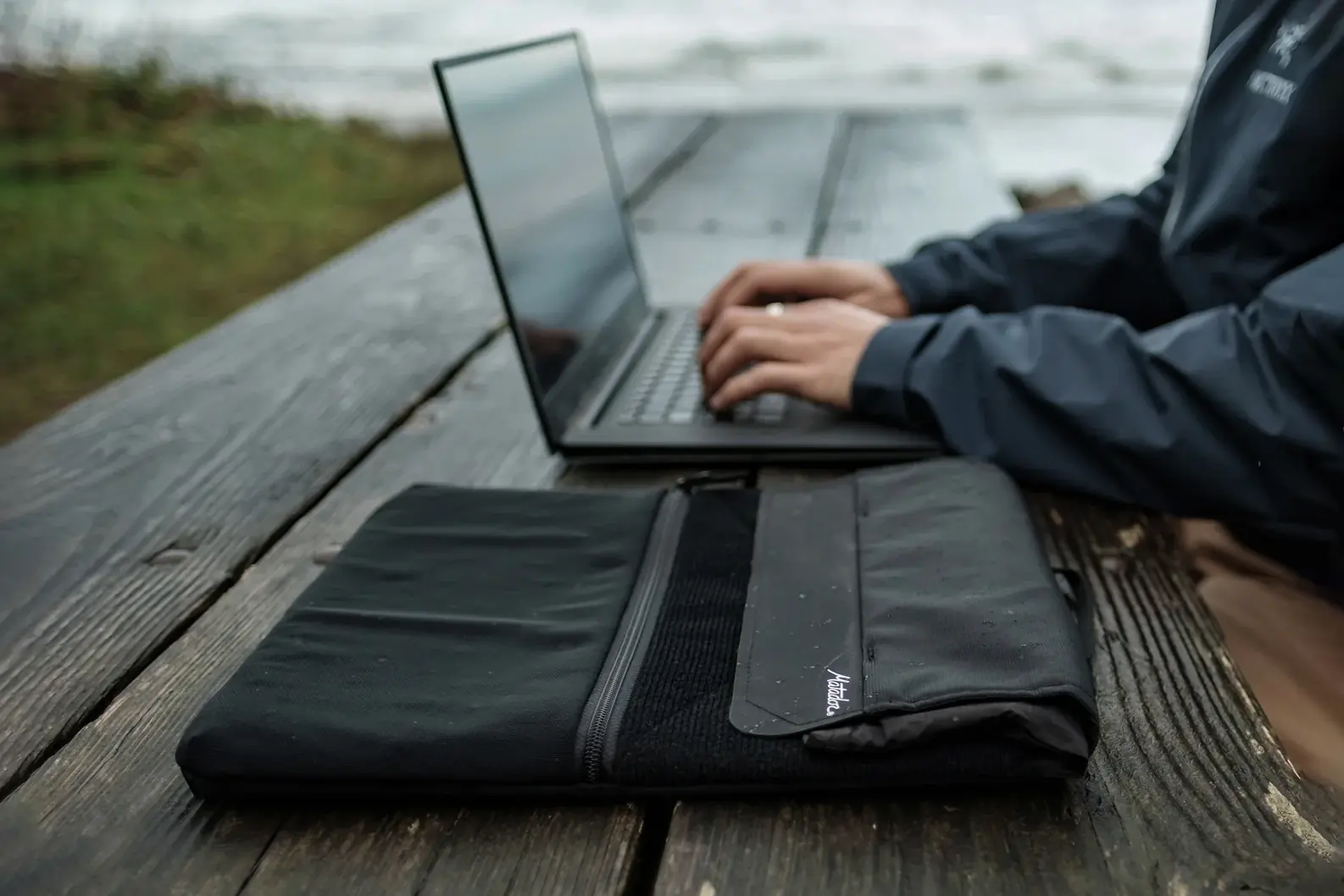 person typing on laptop outside on grey day with Matador laptop base layer in foreground