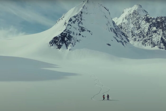 two women are tiny dots against a snowy background with mountains in the background